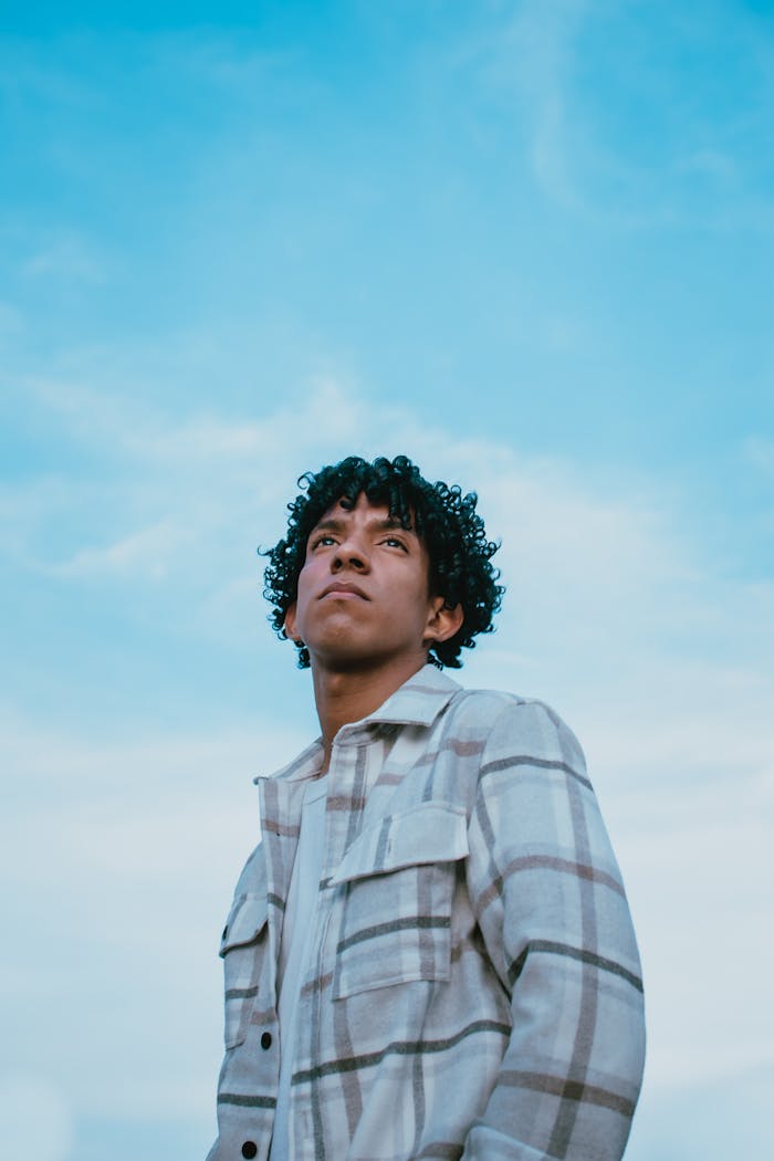 gallery-5 A young man in a plaid jacket looking up against a blue sky. Captivating and stylish fashion portrait.