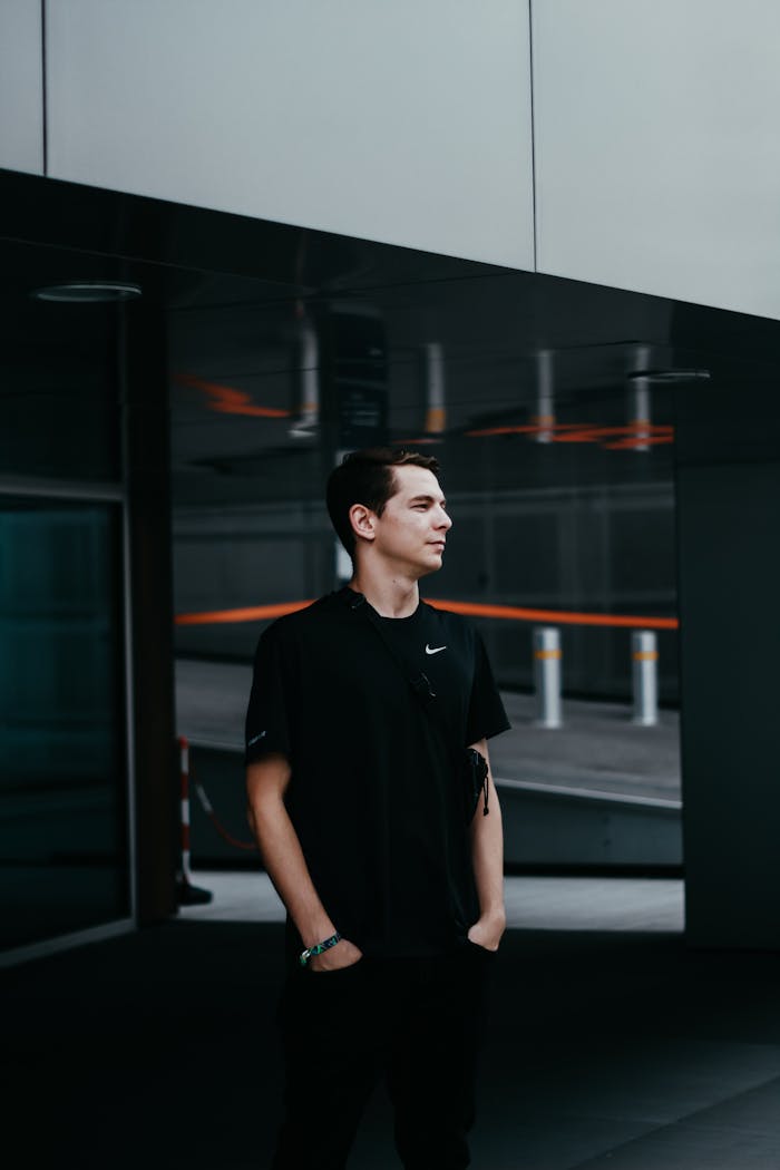 gallery-3 Young man standing outdoors in Berlin with reflective background, casual black attire.