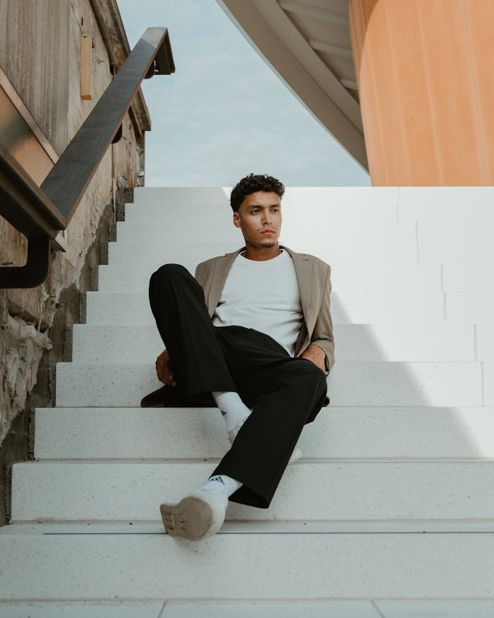 our-services-1 Portrait of a fashionable man sitting on stairs in a modern Berlin setting, exuding confidence and style.