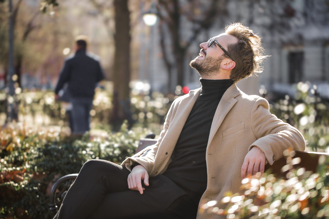services-01 A stylish man in sunglasses relaxes in a city park, basking in the sunlight.