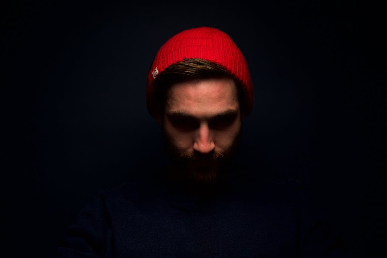 our-services-3 Dramatic low-key portrait of a man in a red beanie, emphasizing shadows and emotion.