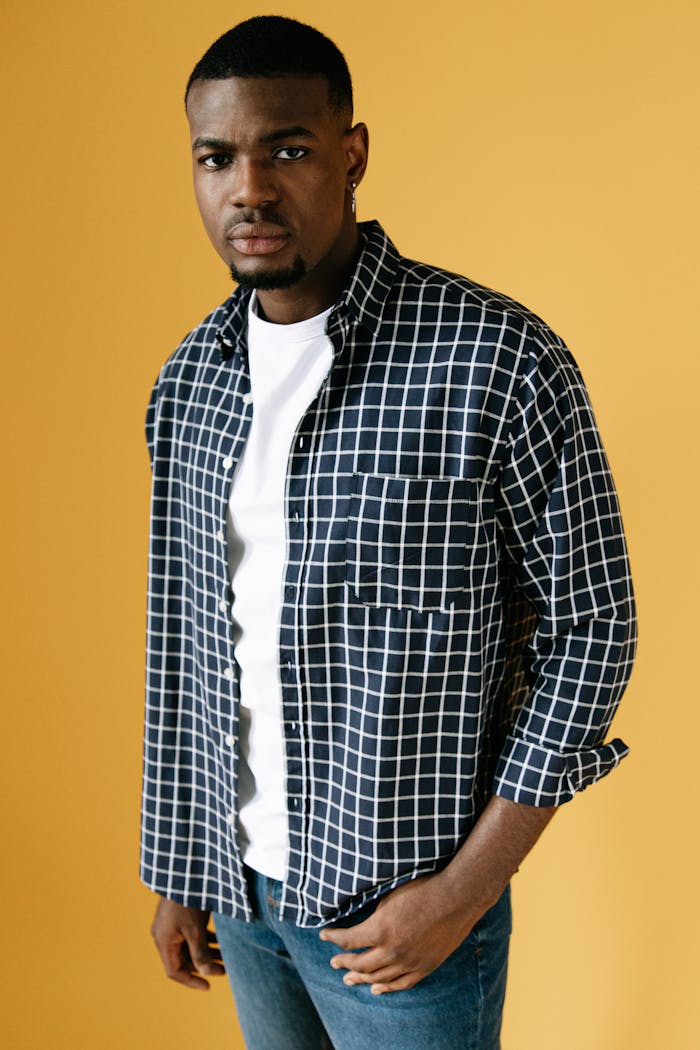 African American man in a checkered shirt poses stylishly against a yellow background.